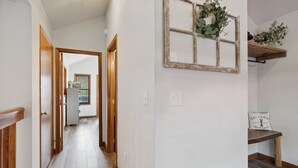 A hallway with wooden flooring, white walls, and a rustic wall decoration.