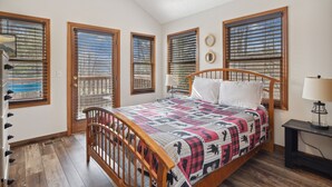 A bedroom with a wooden bed, a nightstand, a lamp, and large windows with blinds.