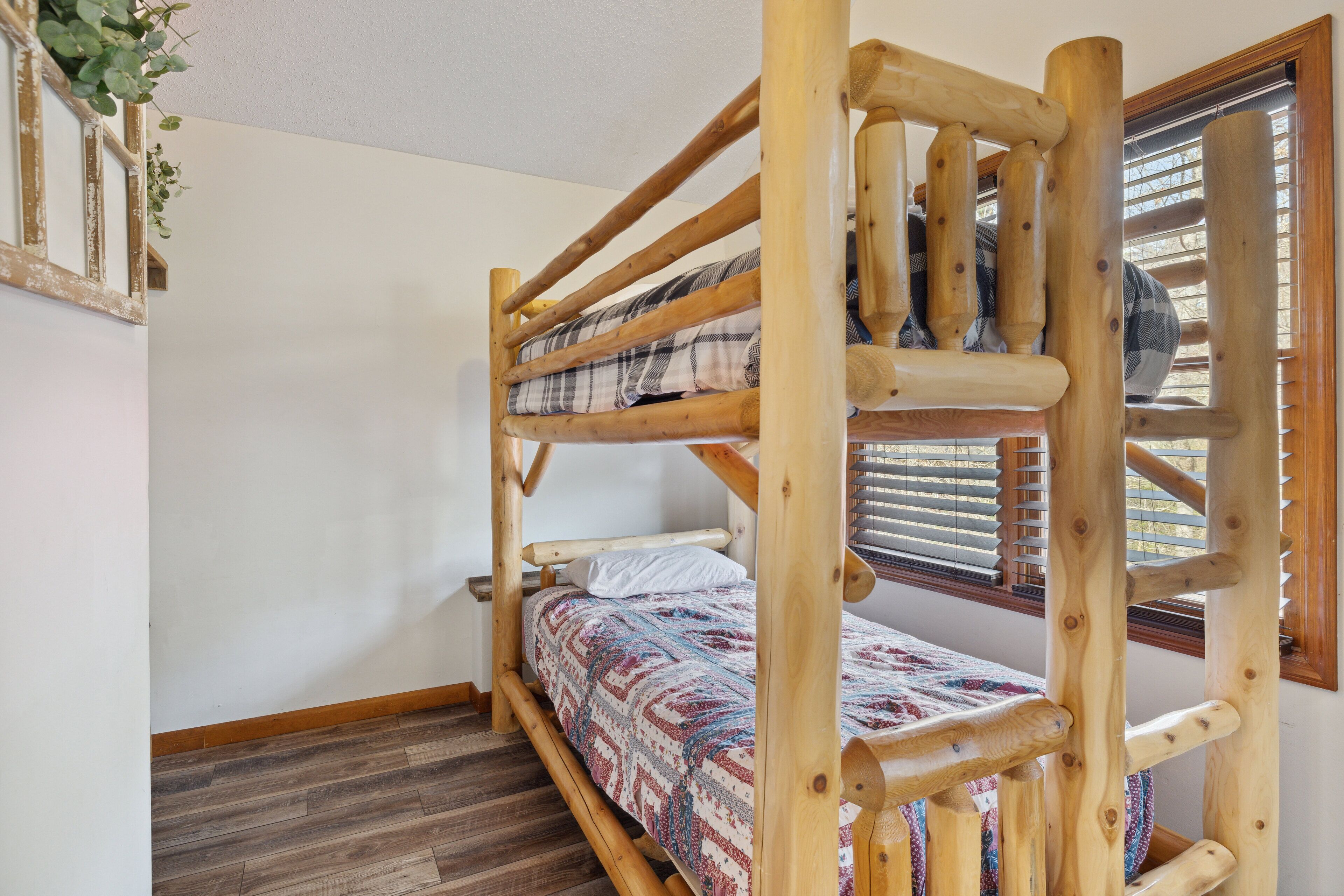 Ein Stockbett mit Holzrahmen, einer gemusterten Bettdecke und einem Fenster mit Jalousien.