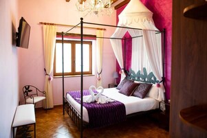Una cama con dosel y cortina blanca, cubrecama morado y decoración con forma de cisne blanco.
