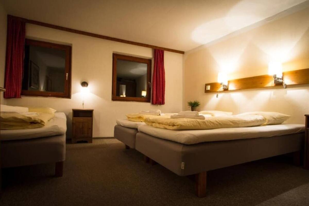 A bedroom with two single beds, a nightstand, a mirror, and a wall-mounted shelf with a lamp.