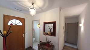 A hallway with a wooden door, a mirror, a small table with a vase, and a ceiling light.