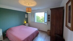 A bedroom with a bed, a bedside table, a window, and a wooden wardrobe.