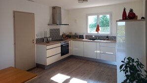 A modern kitchen with white cabinets, a built-in oven, a window with a view, and a wooden floor.