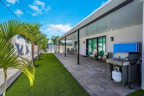 A modern outdoor patio with artificial grass, a barbecue grill, and seating. - Screened Pool Courtyard • Hot Tub • Beach Nearby (Sarasota)