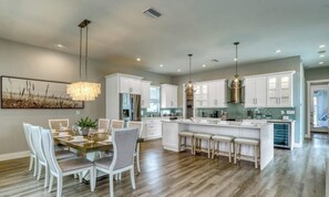 A spacious kitchen with white cabinetry, a central island with stools, pendant lighting, and a dining area with chairs. - Screened Pool Courtyard • Hot Tub • Beach Nearby (Sarasota)