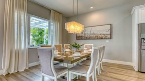 A dining area with a wooden table set for six, surrounded by chairs, a chandelier, and a painting on the wall.