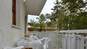 Ein Balkon mit Tisch für zwei Personen, weißen Stühlen und einem Korbwannenmöbel.