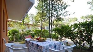 An outdoor patio with a table covered in a patterned tablecloth, two white plastic chairs, and a bowl of fruit. - Choose our cozy garden (Lignano Sabbiadoro)