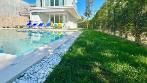 A modern house with a swimming pool, a covered patio, and a well-maintained lawn.