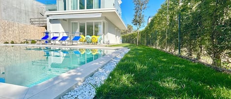 Une maison moderne dotée d’une piscine, d’un patio couvert et d’une pelouse bien entretenue.