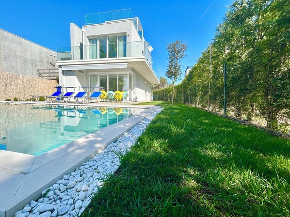 Une maison moderne dotée d’une piscine, d’un patio couvert et d’une pelouse bien entretenue.