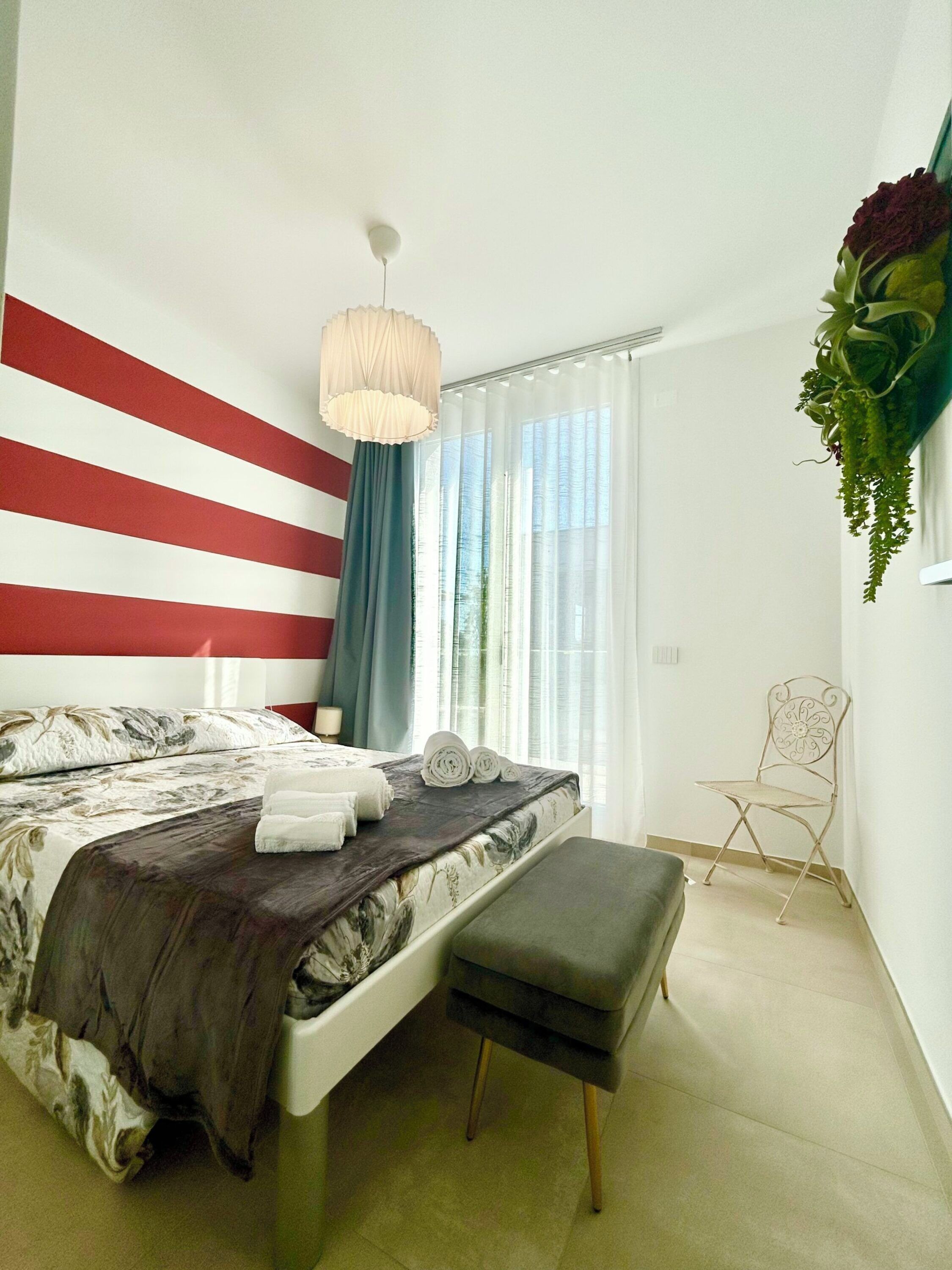 A bedroom with a bed, a bench, a hanging plant, and a chair.