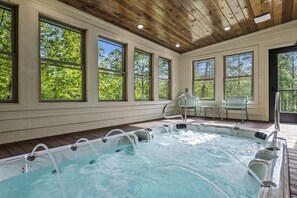 Un jacuzzi con terraza de madera, ventanas amplias y un banco.