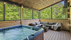 A wooden deck with a hot tub, a sofa, and a wicker coffee table.
