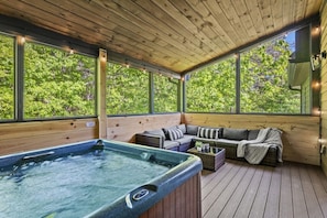 A wooden deck with a hot tub, a sofa, and a wicker coffee table.