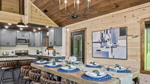 A modern kitchen with grey cabinets, a central island, and a dining area set for six with leather chairs.