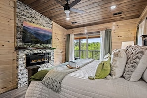 A cozy room with a fireplace, a bed with pillows, a TV mounted on a wall, and a balcony with a view.