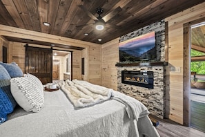 Une chambre confortable avec une cheminée, un lit recouvert d’une couverture blanche et un téléviseur fixé au mur.