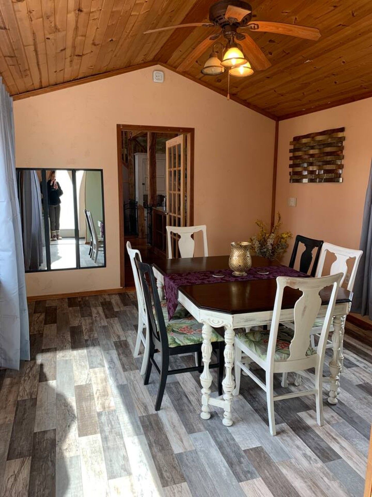 A dining area with a wooden ceiling, a table with chairs, and a mirror on the wall.