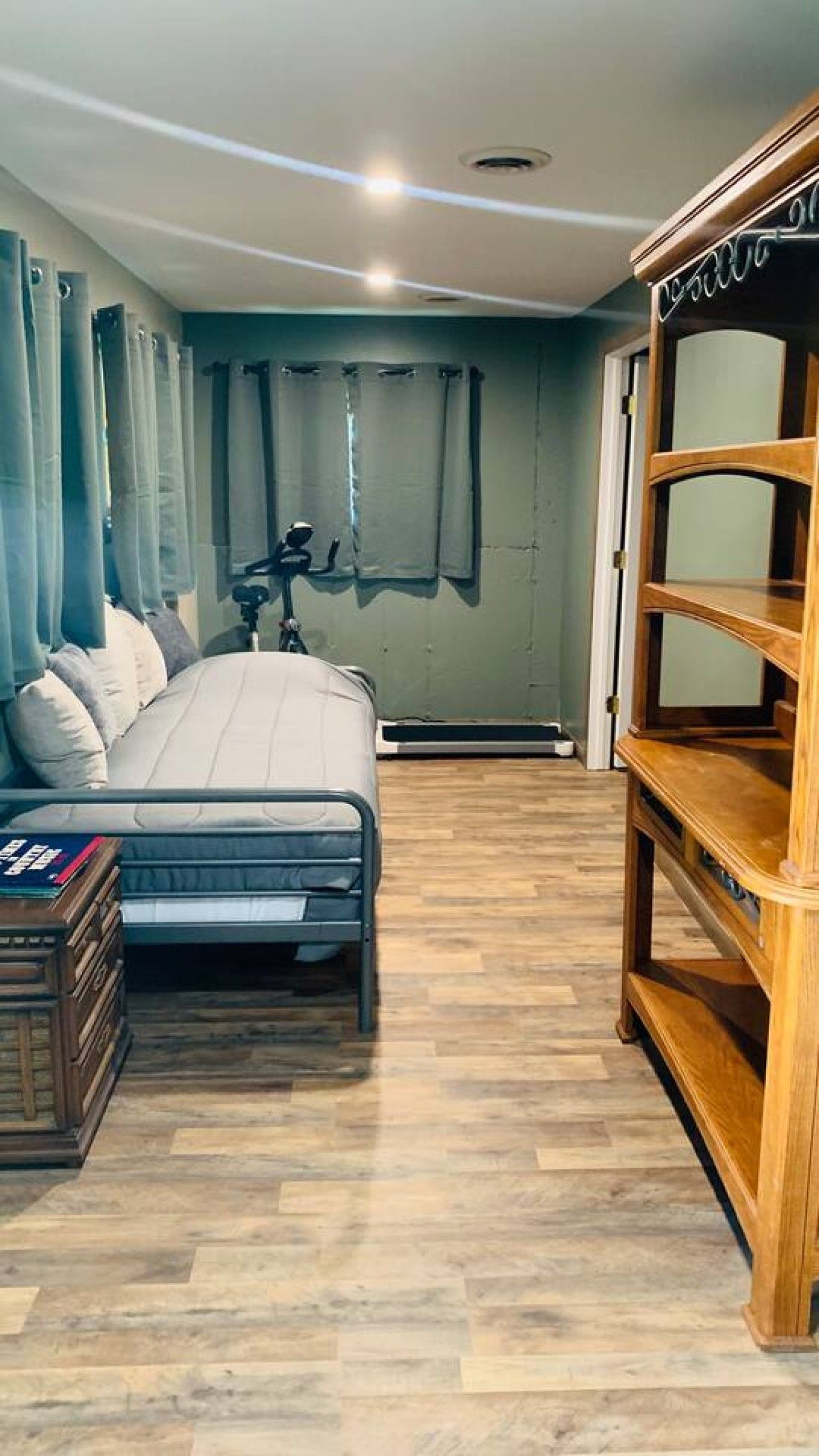 Un dormitorio con una cama, cortinas, un estante de madera y una cámara sobre un trípode.