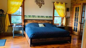 A bedroom with a wooden bed, two bedside tables, a nightstand, a window with yellow curtains, and a wall-mounted decorative piece.