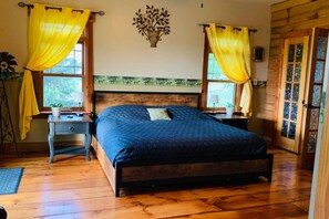 Quarto com cama de madeira, duas mesinhas de cabeceira, um criado-mudo, janela com cortinas amarelas e um objeto decorativo na parede.