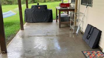 A covered patio area with a concrete floor, a grill, a table with a red box, and a hammock.