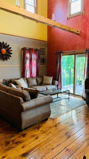 A living room with a sectional sofa, a glass coffee table, and a view of a green outdoor area through large windows.