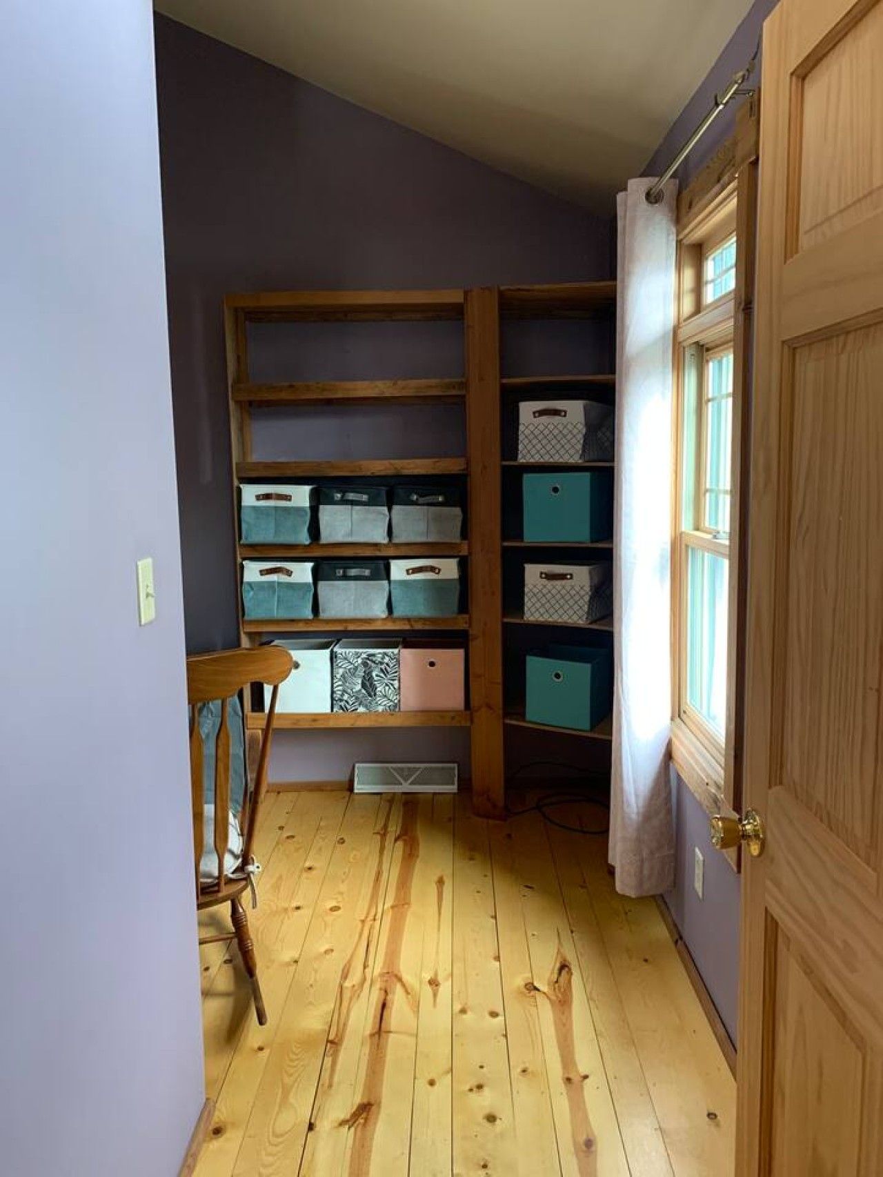 Un pasillo con suelo de madera, una estantería empotrada con cajas de almacenamiento y una puerta con ventanal.