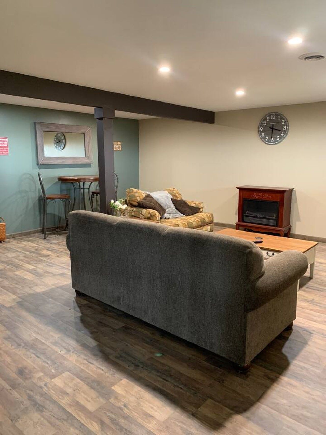 A room with a sofa, a wooden coffee table, a clock on the wall, and a small table with chairs.