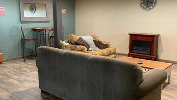 A room with a sofa, a wooden coffee table, a clock on the wall, and a small table with chairs.