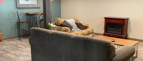 Ein Zimmer mit einer Couch, einem Holztisch, einer Wanduhr und einem kleinen Tisch mit Stühlen.