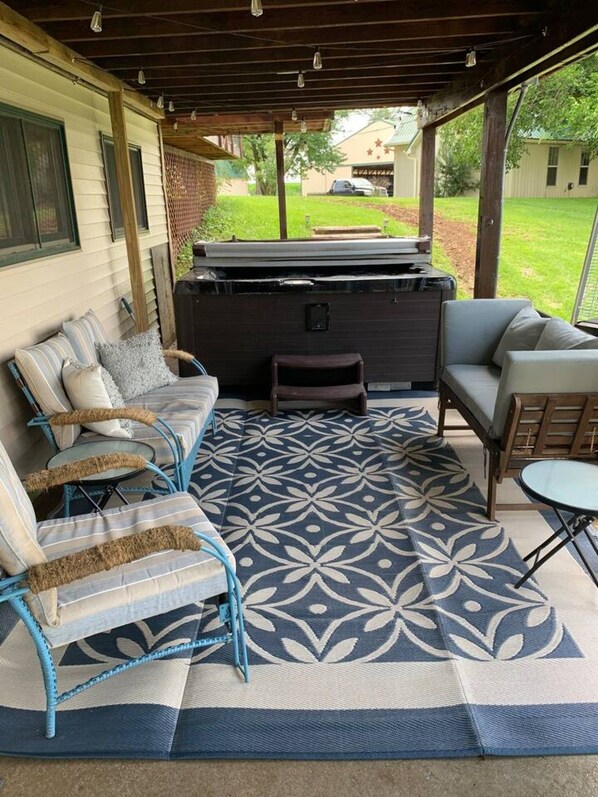 An outdoor patio with a hot tub, seating area, and a patterned rug.