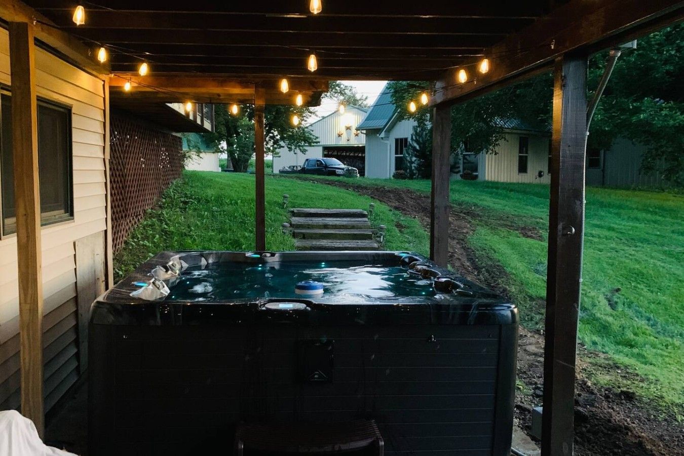 Een hottub onder een overdekt terras, omringd door een gazon en een huis op de achtergrond.