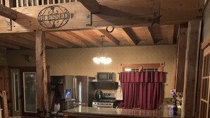 Un salon chaleureux avec un canapé en cuir marron, un plafond en bois et un coin cuisine à l’arrière-plan.