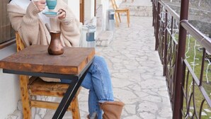 A person seated at a wooden table on a stone-paved balcony with metal railings, holding a cup. - Restland Dilijan Family Hotel  (Dilijan)