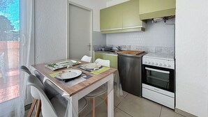 Et lille køkken med spisebord, stole, køleskab, komfur og et vindue med udsigt.