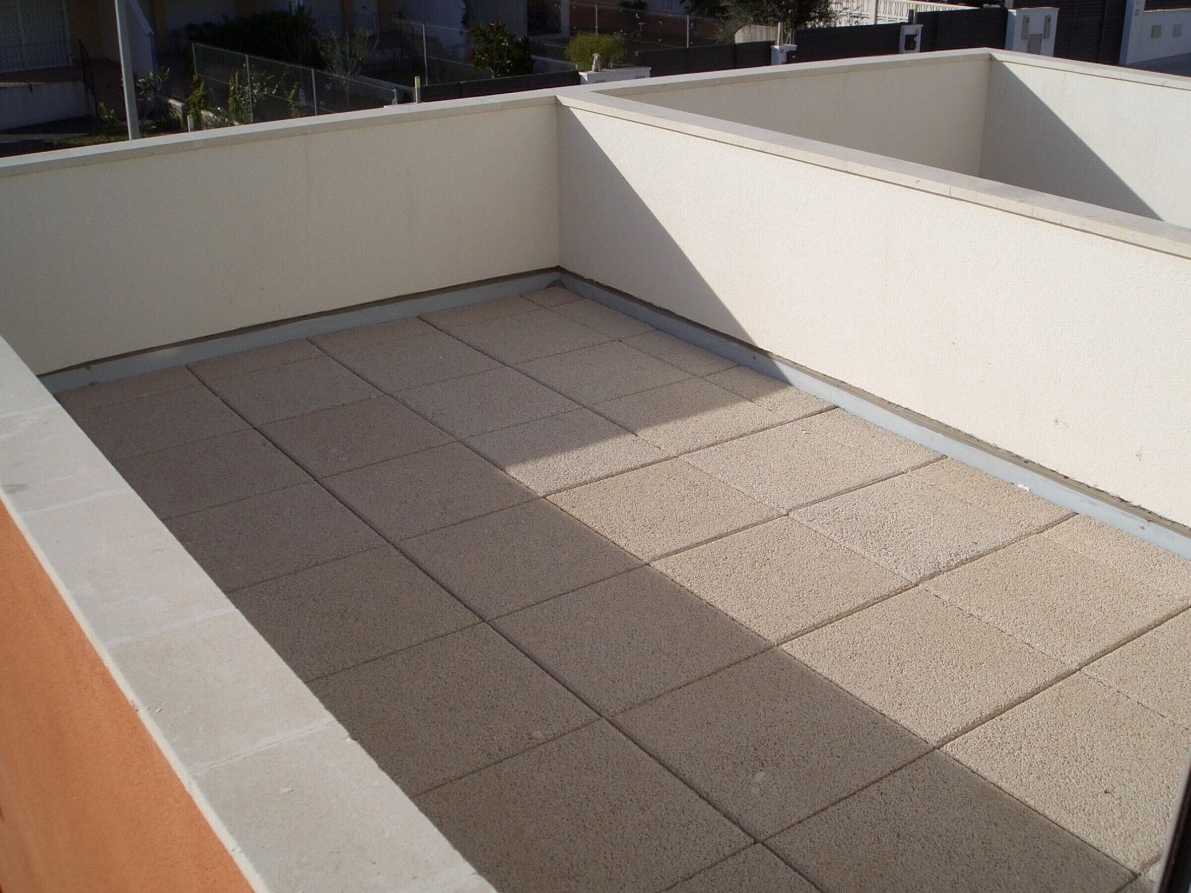 A rooftop terrace with a tiled floor and a white wall.