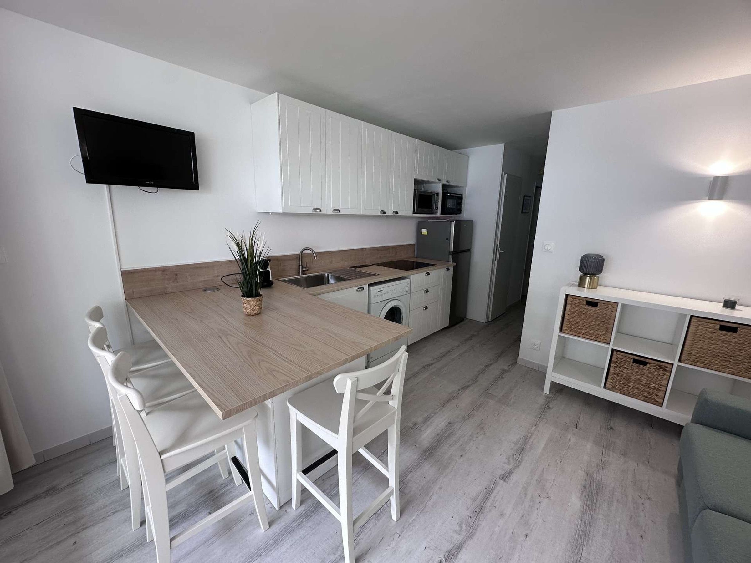 Cocina compacta con armarios blancos, encimera de madera, microondas integrado y lavadora.
