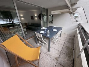 A balcony with a dining table set for two, a yellow chair, and a sofa. - 2-room apartment with pool, tennis and private parking 50m from the beach (Port Camargue)
