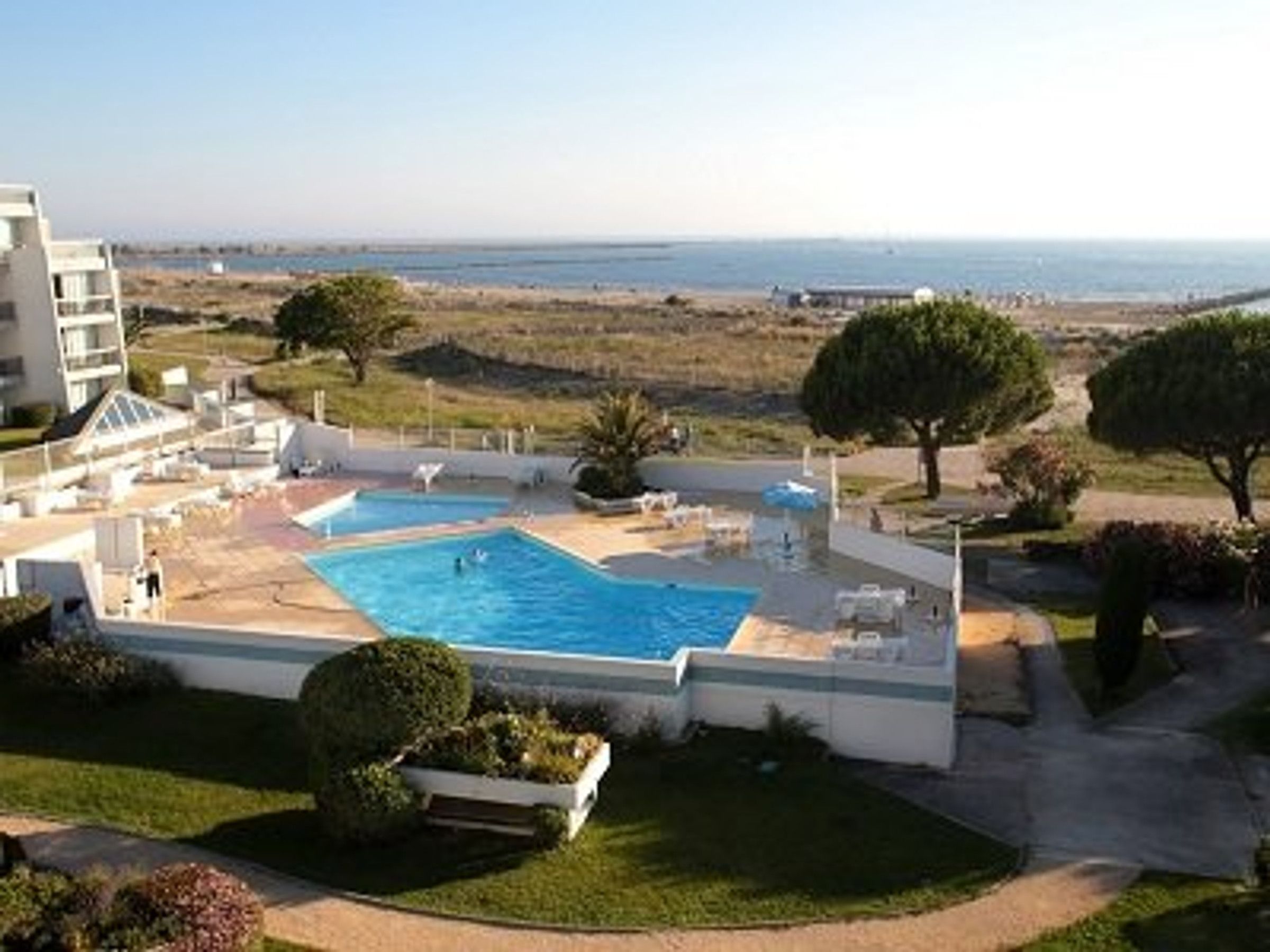 A pool area with a view of the sea, surrounded by greenery and a building.