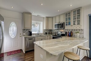 A modern kitchen with a central island, stainless steel appliances, and a large window. - 833 Ocean Cove - Luxury home Free Tennis/Pickleball daily (Hilton Head Island)