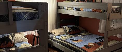 A room with three bunk beds, wooden flooring, and a window with white curtains.