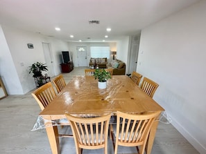 Un comedor con mesa de madera, sillas, una planta en maceta y un televisor al fondo.