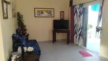 A living room with a sofa, a TV on a stand, a potted plant, and a painting on the wall.