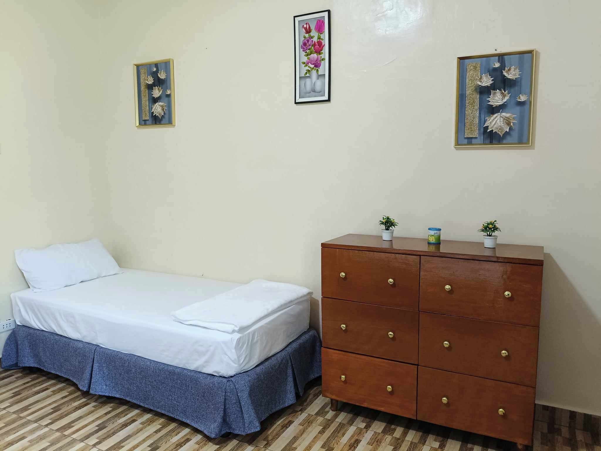 A bedroom with a bed, a dresser, and three wall-mounted pictures.