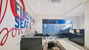 A modern living room with a sofa, coffee table, and a wall with 'FIND YOUR SEAT' text. - Hotel Veridian (Lucknow)