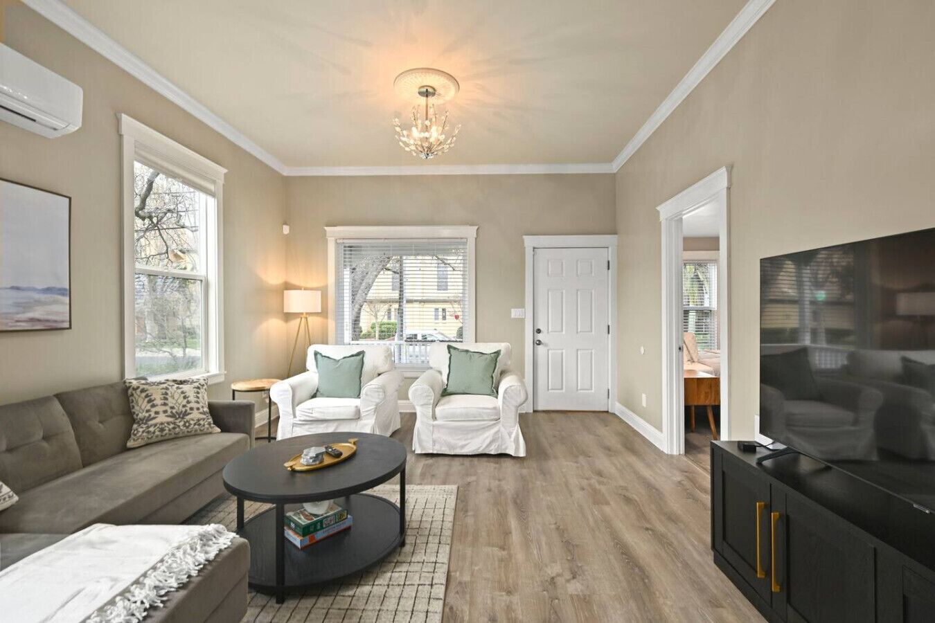 A living room with a sofa, two white armchairs, a coffee table, a TV, and a chandelier.