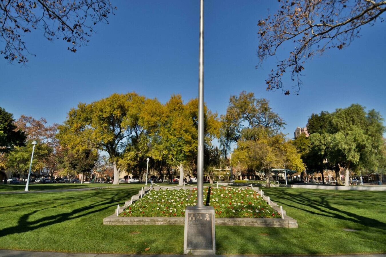 Een park met een centraal monument, verzorgd gras en bomen met herfstkleuren.